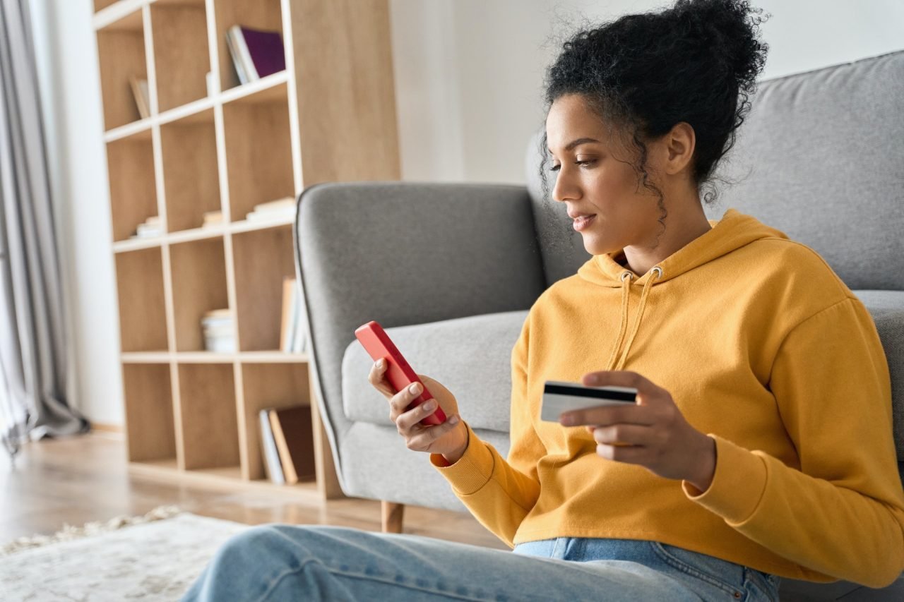 young-adult-african-american-girl-sitting-indoors-doing-mobile-payment-online-.jpg